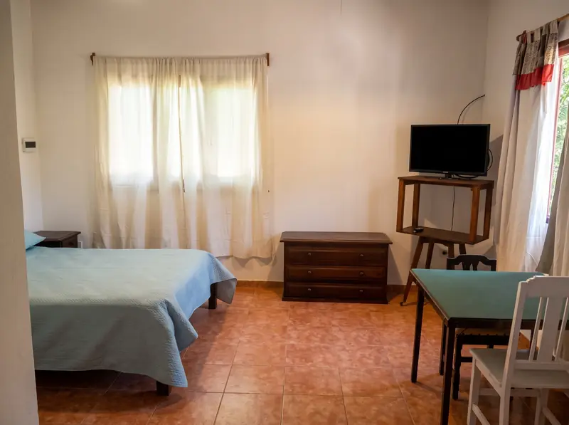 Cama doble con acolchado celeste, cómoda y mesa con sillas