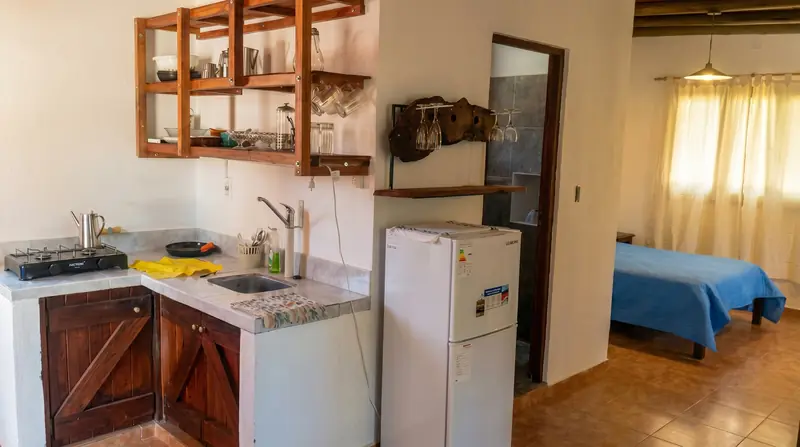 Cocina con anafe, bacha y heladera, con la cama al fondo